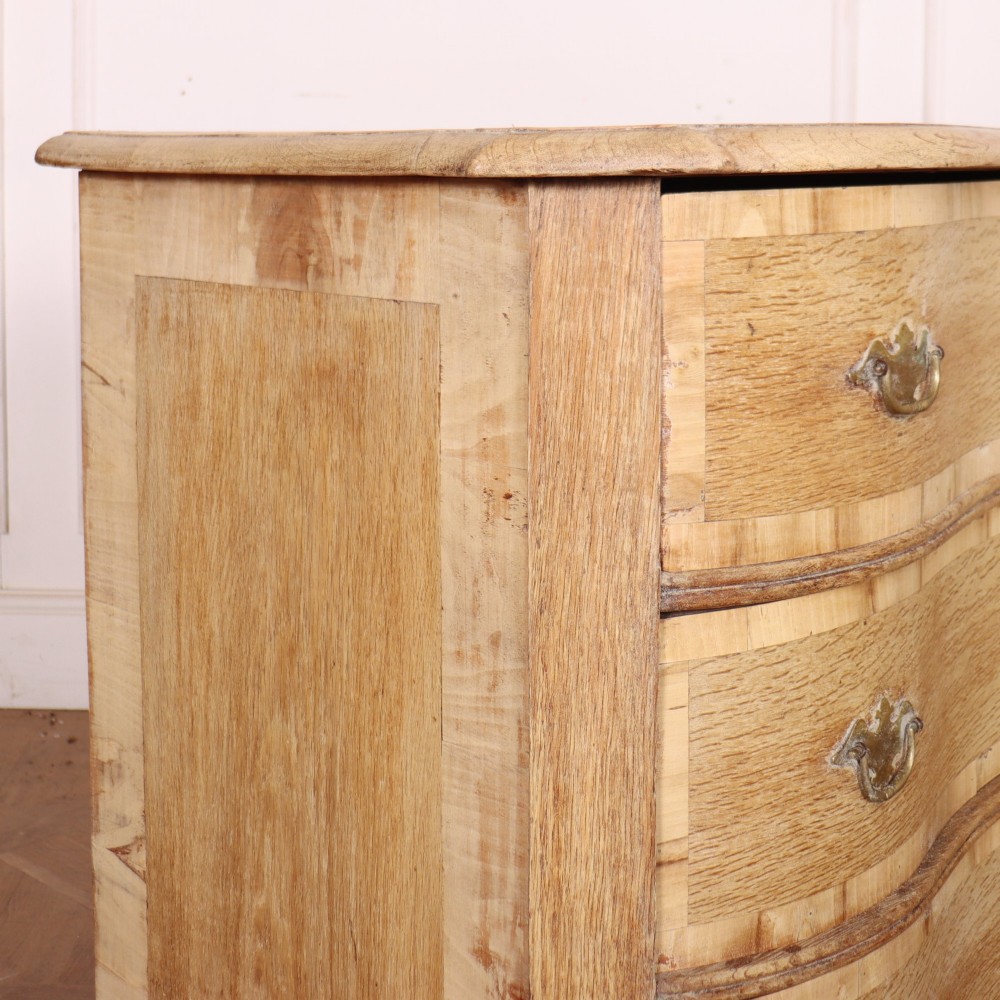 An Austrian bleached oak commode featuring a serpentine front, three drawers with crossbanded borders, brass escutcheons, handles, and turned feet. View IX