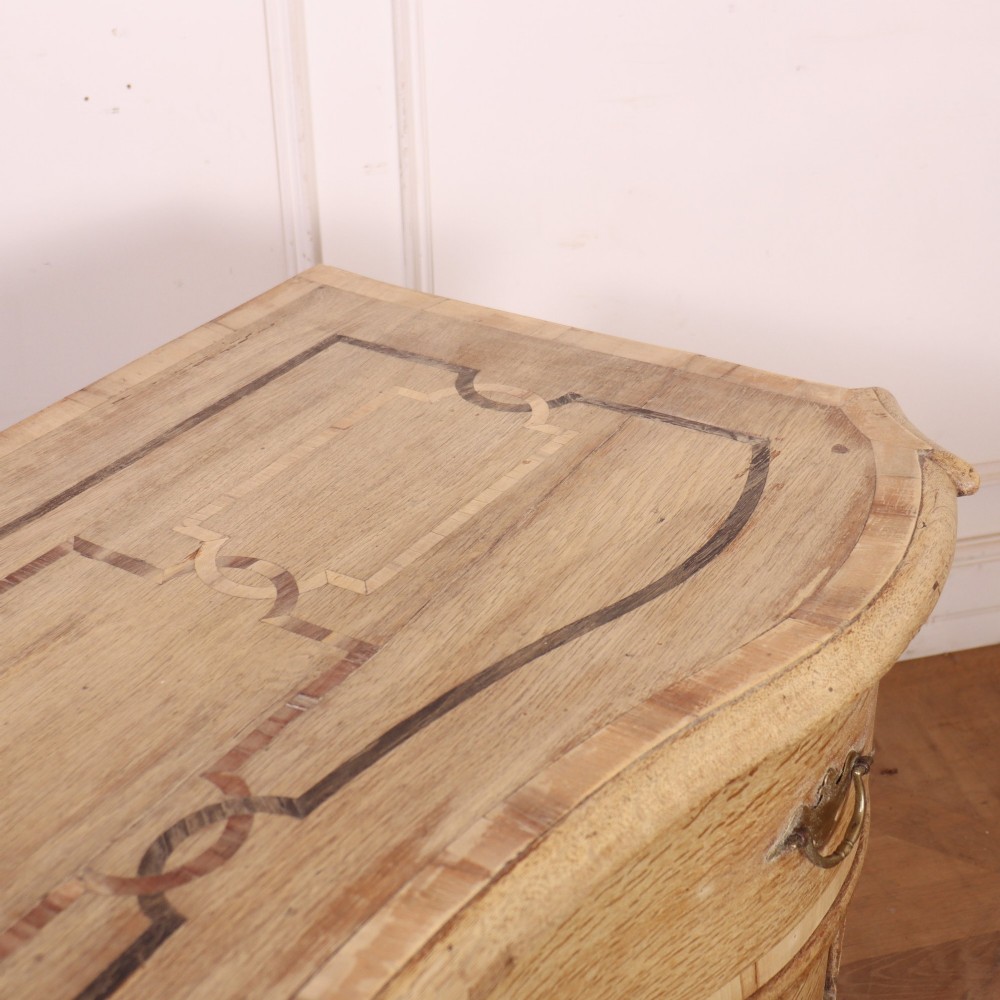 An Austrian bleached oak commode featuring a serpentine front, three drawers with crossbanded borders, brass escutcheons, handles, and turned feet. View XII