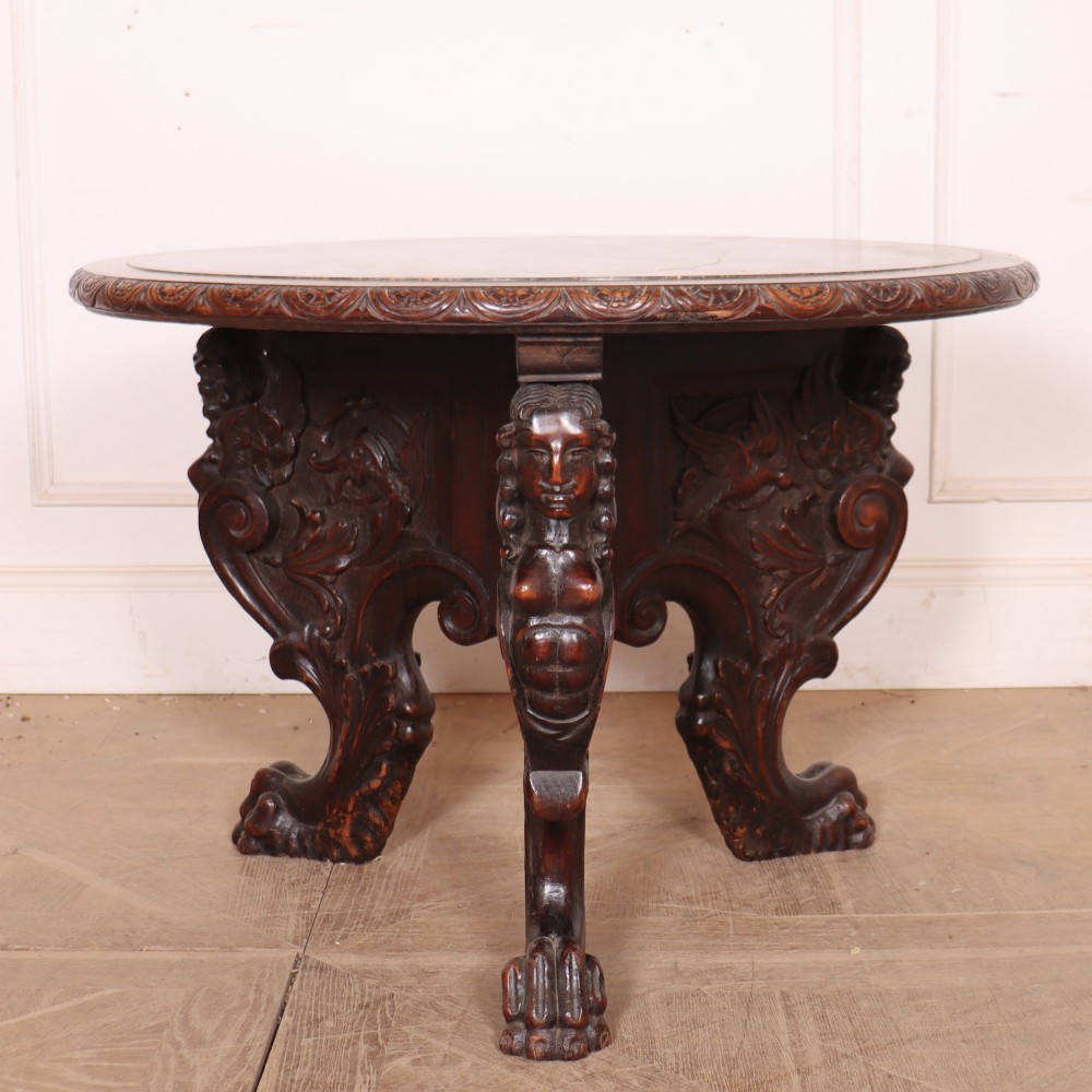 A circular dark wood lamp table featuring an inset dark marble top, intricately carved floral borders, and carved caryatid legs resting on paw feet. View VI