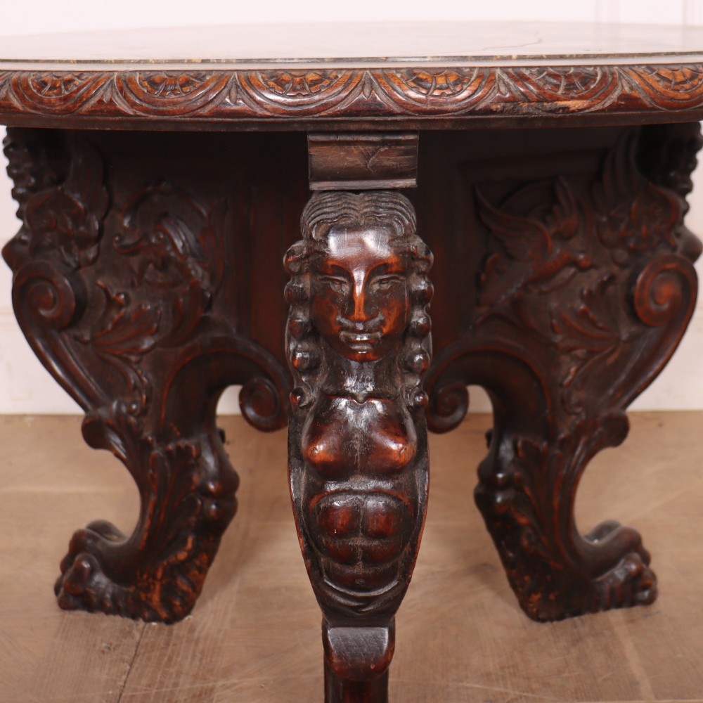 A circular dark wood lamp table featuring an inset dark marble top, intricately carved floral borders, and carved caryatid legs resting on paw feet. View VII