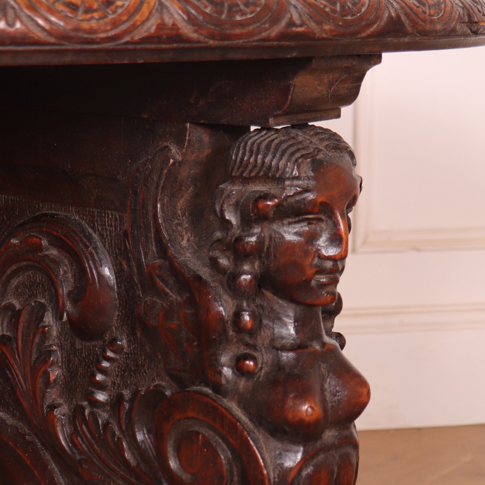 A circular dark wood lamp table featuring an inset dark marble top, intricately carved floral borders, and carved caryatid legs resting on paw feet. View X
