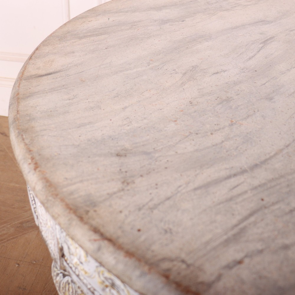 A Swedish Gustavian style circular side table featuring a distressed off-white painted finish, carved wave pattern apron, fluted legs, and an X-shaped stretcher with a central urn finial. View VI