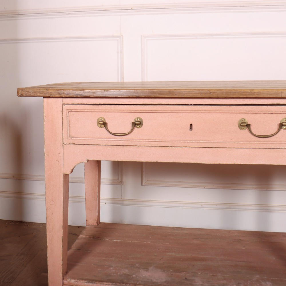 A Scottish farmhouse potboard dresser base with a painted pink frame, wide drawers fitted with brass handles, and an open lower wooden shelf. View II