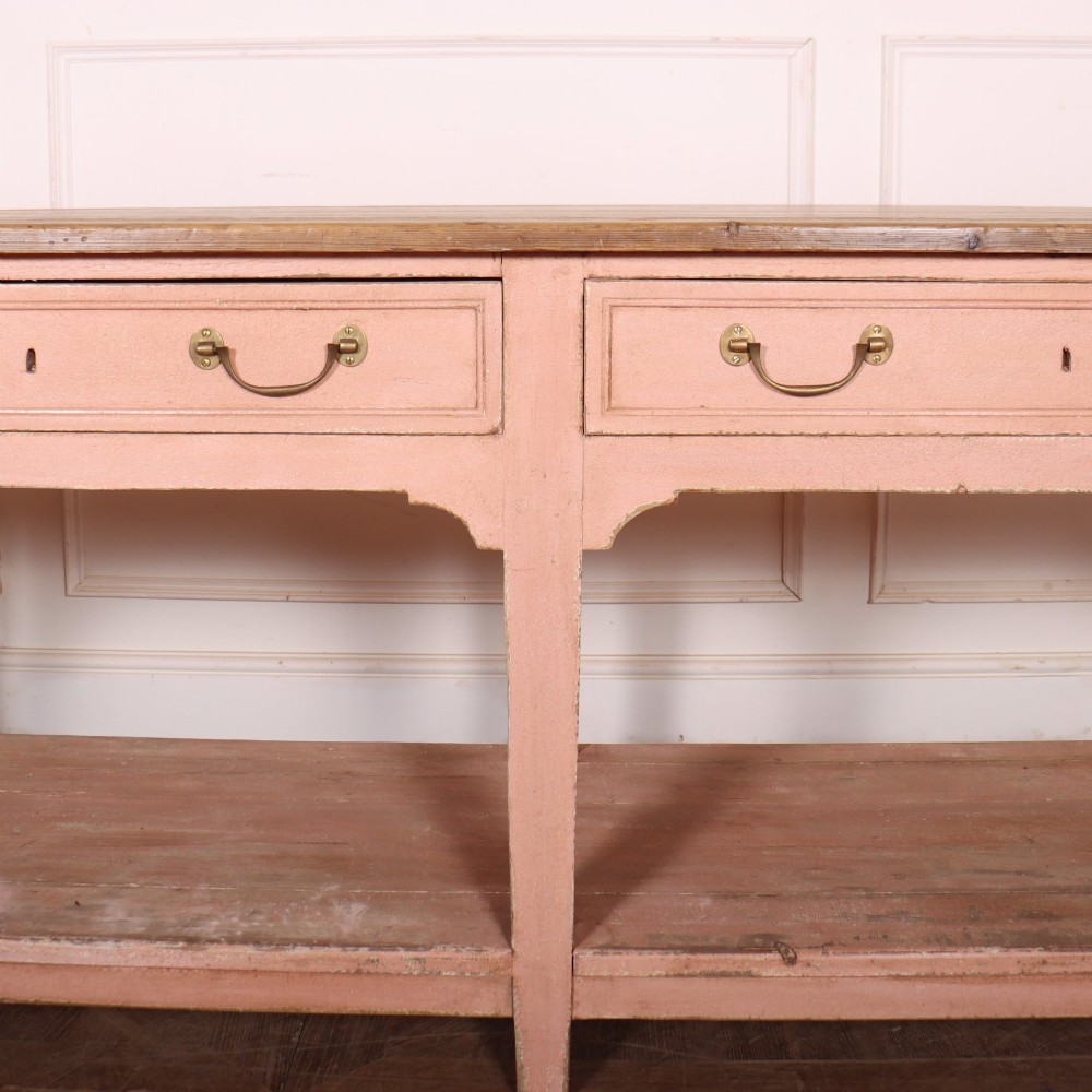 A Scottish farmhouse potboard dresser base with a painted pink frame, wide drawers fitted with brass handles, and an open lower wooden shelf. View IV