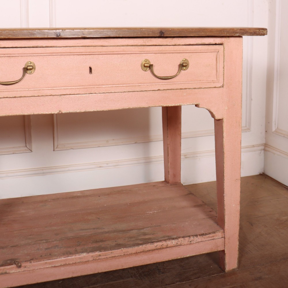 A Scottish farmhouse potboard dresser base with a painted pink frame, wide drawers fitted with brass handles, and an open lower wooden shelf. View VI