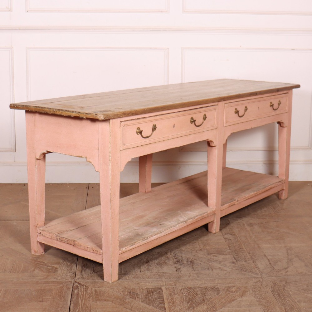 A Scottish farmhouse potboard dresser base with a painted pink frame, wide drawers fitted with brass handles, and an open lower wooden shelf. View VIII