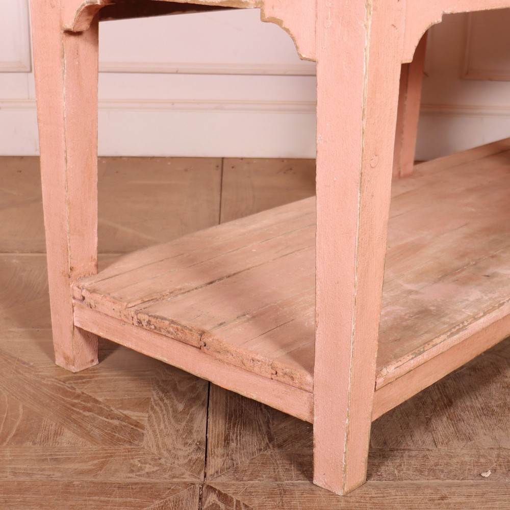 A Scottish farmhouse potboard dresser base with a painted pink frame, wide drawers fitted with brass handles, and an open lower wooden shelf. View IX
