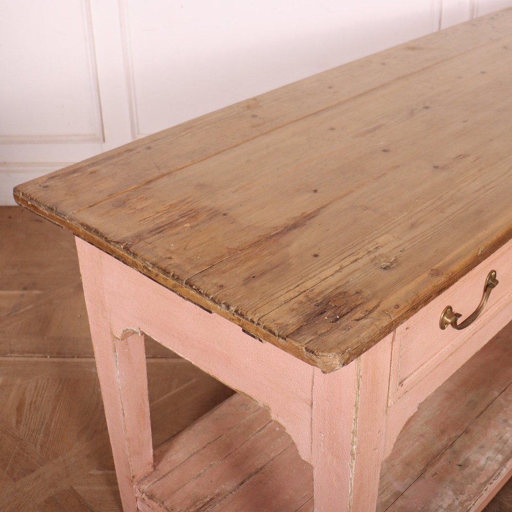 A Scottish farmhouse potboard dresser base with a painted pink frame, wide drawers fitted with brass handles, and an open lower wooden shelf. View XI
