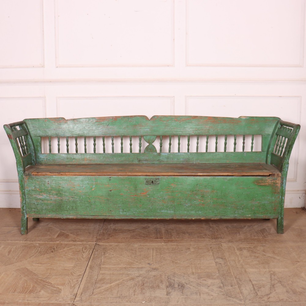 An antique green painted pine settle bench featuring a spindle backrest and a hinged storage seat base.