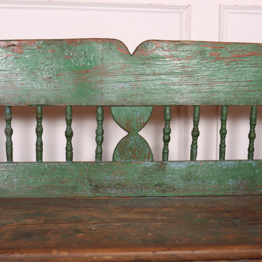 An antique green painted pine settle bench featuring a spindle backrest and a hinged storage seat base. View IV