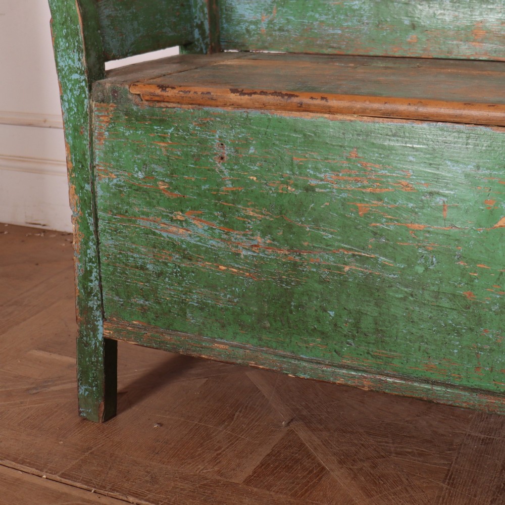 An antique green painted pine settle bench featuring a spindle backrest and a hinged storage seat base. View V
