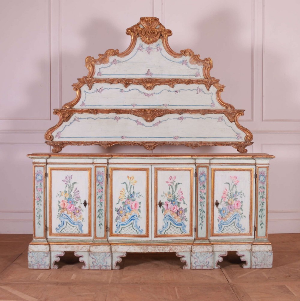 An eighteenth-century Venetian painted sideboard featuring floral polychrome panels, giltwood mouldings, and a tiered decorative pediment.
