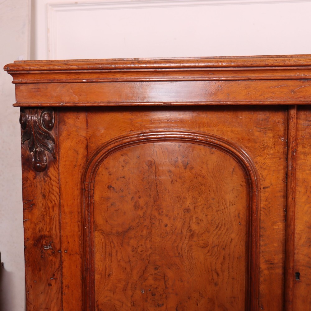 An antique English burr walnut dresser base featuring six arched cupboard doors with hand-carved decorative corbels along the top moulding. View II