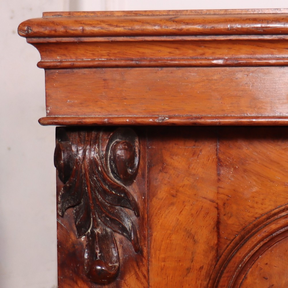 An antique English burr walnut dresser base featuring six arched cupboard doors with hand-carved decorative corbels along the top moulding. View III