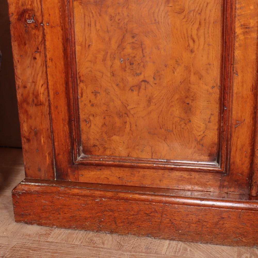 An antique English burr walnut dresser base featuring six arched cupboard doors with hand-carved decorative corbels along the top moulding. View IV