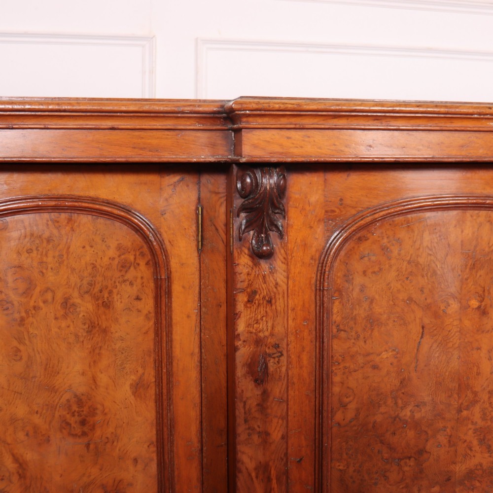 An antique English burr walnut dresser base featuring six arched cupboard doors with hand-carved decorative corbels along the top moulding. View V