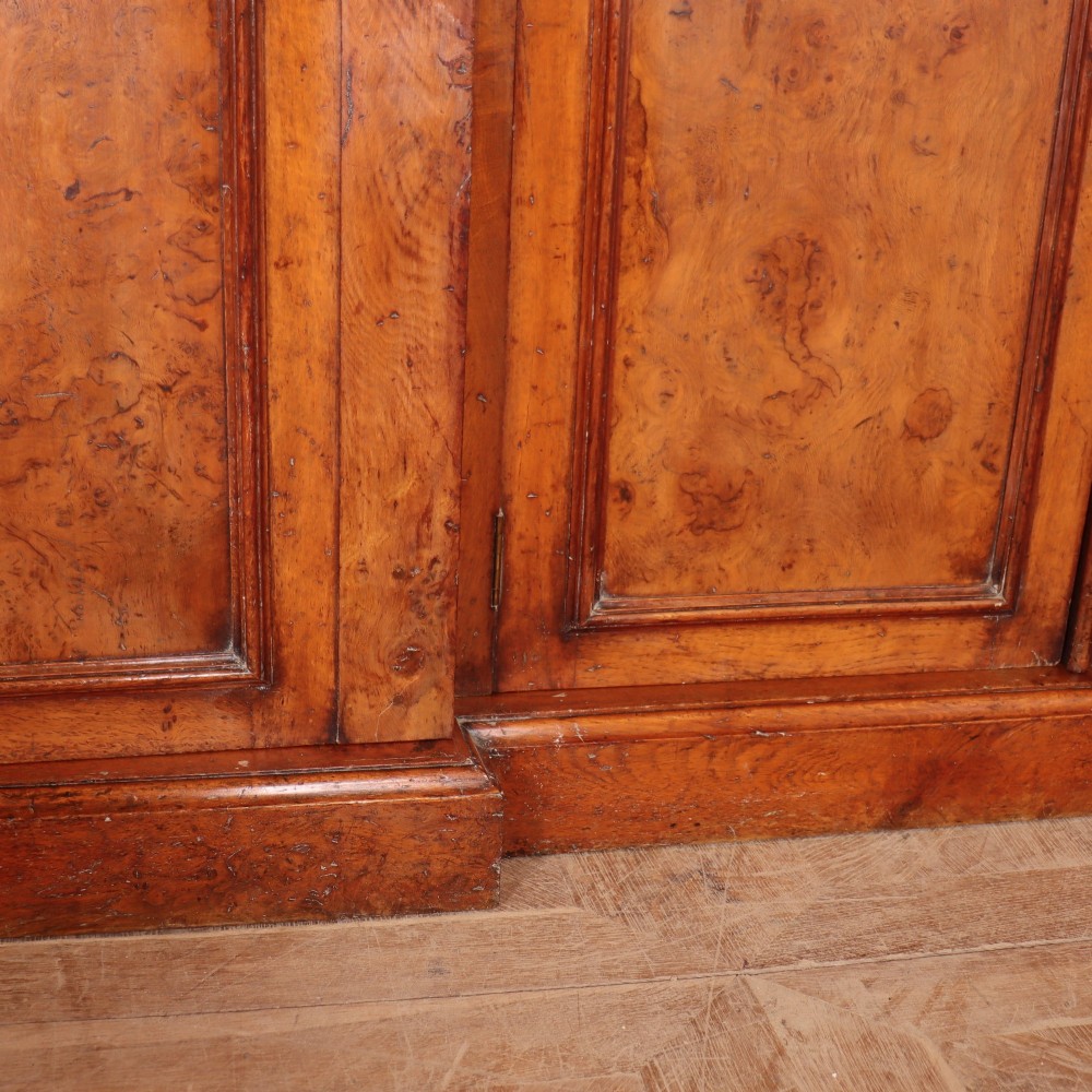 An antique English burr walnut dresser base featuring six arched cupboard doors with hand-carved decorative corbels along the top moulding. View VI