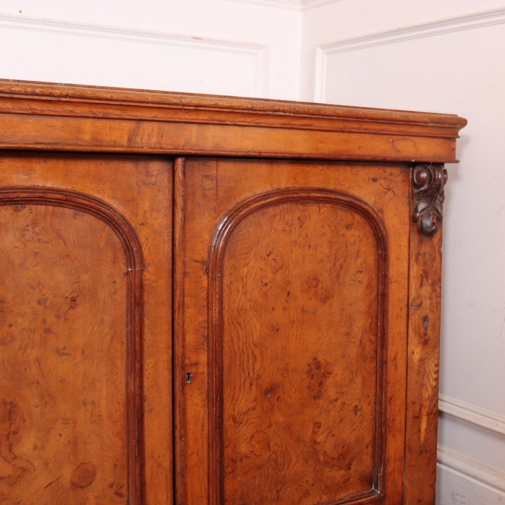 An antique English burr walnut dresser base featuring six arched cupboard doors with hand-carved decorative corbels along the top moulding. View VII