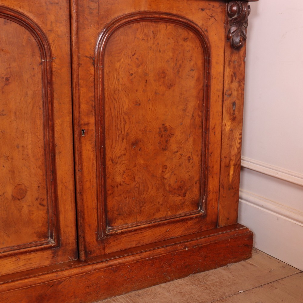 An antique English burr walnut dresser base featuring six arched cupboard doors with hand-carved decorative corbels along the top moulding. View VIII
