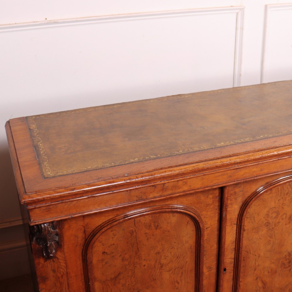 An antique English burr walnut dresser base featuring six arched cupboard doors with hand-carved decorative corbels along the top moulding. View XI