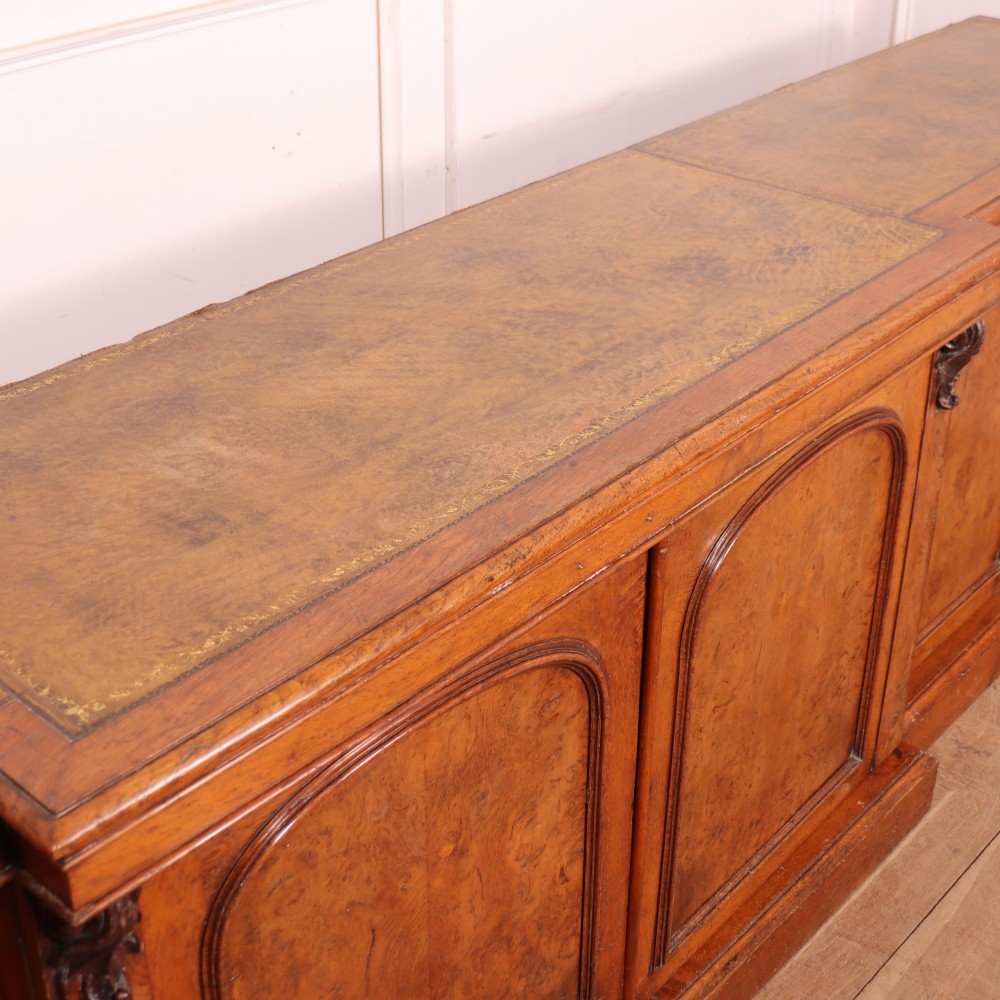 An antique English burr walnut dresser base featuring six arched cupboard doors with hand-carved decorative corbels along the top moulding. View XII