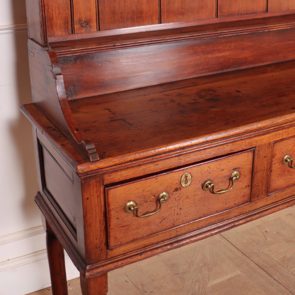 An antique English pine kitchen dresser featuring an open tiered plate rack above three drawers with brass handles, resting on slender turned legs. View VIII