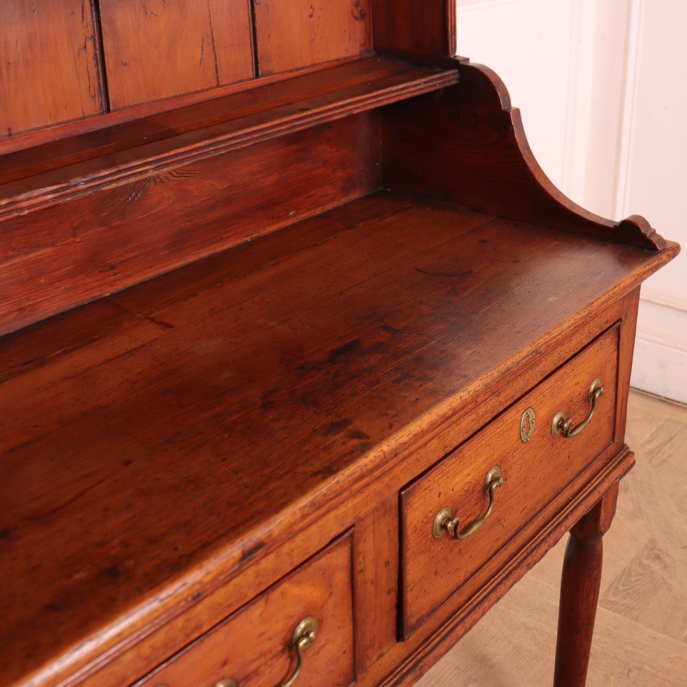 An antique English pine kitchen dresser featuring an open tiered plate rack above three drawers with brass handles, resting on slender turned legs. View IX