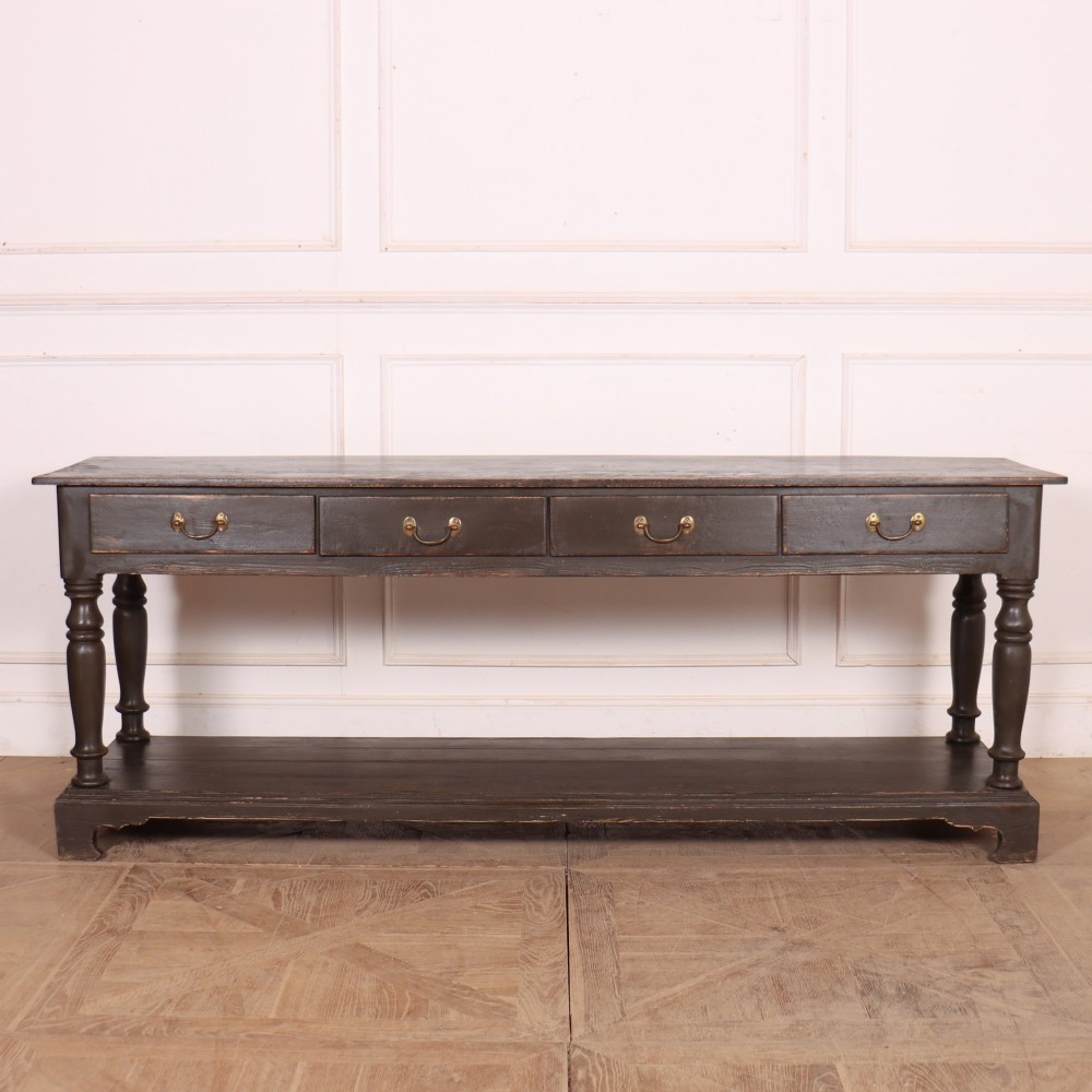 An antique dark grey painted English potboard dresser base featuring four drawers with brass handles, turned legs, and an open lower shelf.