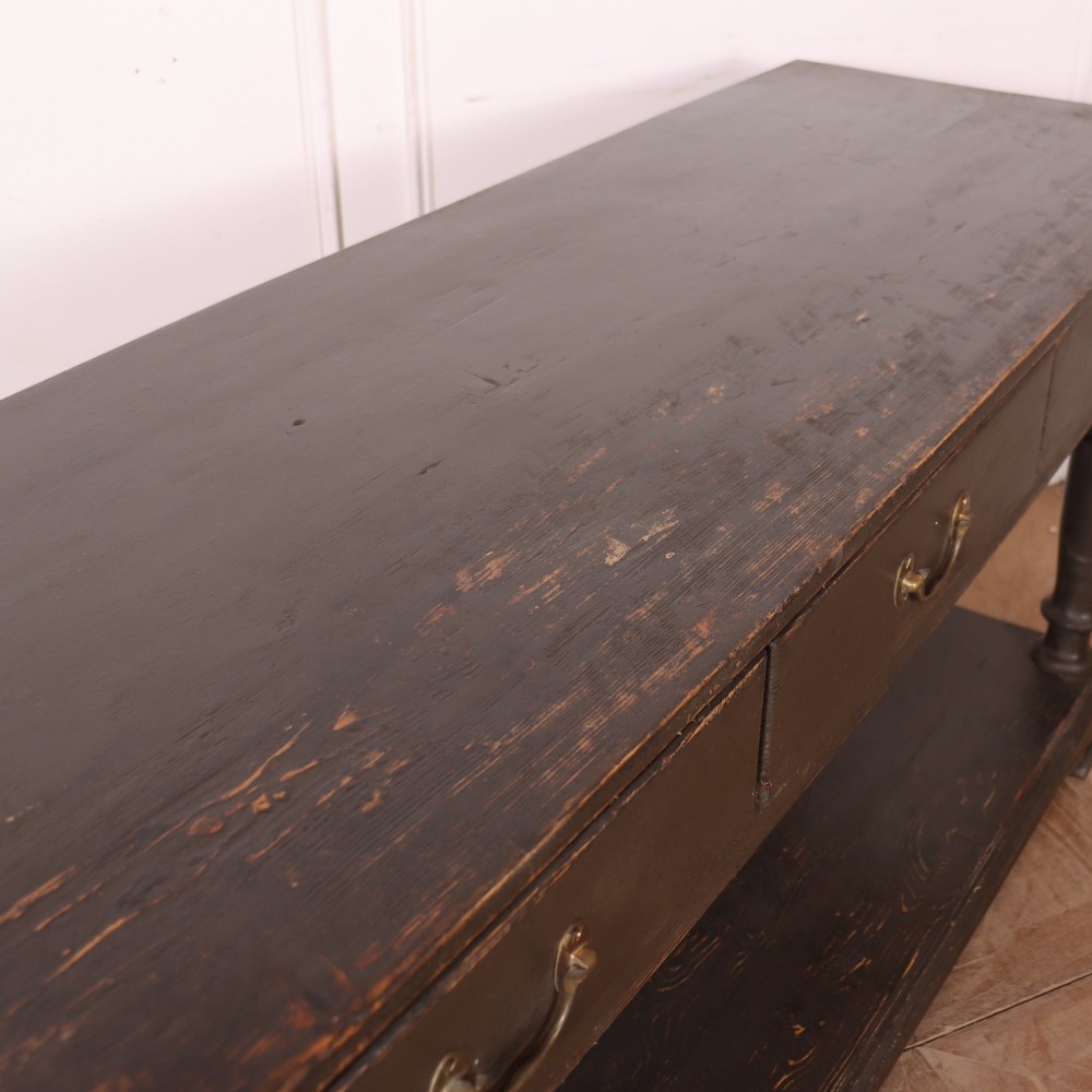 An antique dark grey painted English potboard dresser base featuring four drawers with brass handles, turned legs, and an open lower shelf. View X