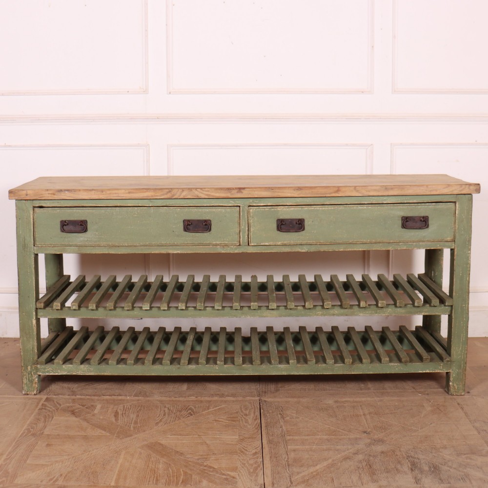 A rustic green painted Scottish dresser base with an unpainted pine top, two drawers with iron metal drop handles, and two slatted lower shelves.