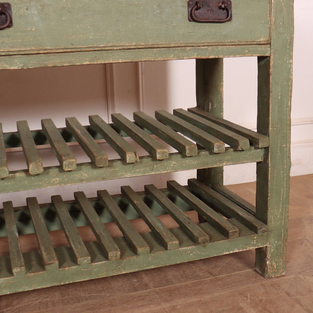 A rustic green painted Scottish dresser base with an unpainted pine top, two drawers with iron metal drop handles, and two slatted lower shelves. View VII