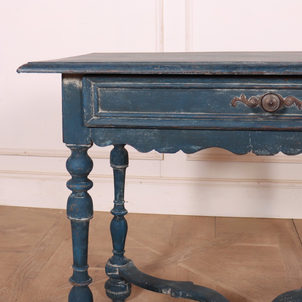 A rectangular blue painted wooden lamp table featuring turned legs, a single drawer with a metal pull, a scalloped apron, and a curved X-shaped stretcher. View II