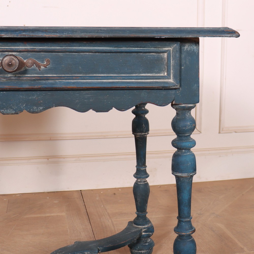 A rectangular blue painted wooden lamp table featuring turned legs, a single drawer with a metal pull, a scalloped apron, and a curved X-shaped stretcher. View IV