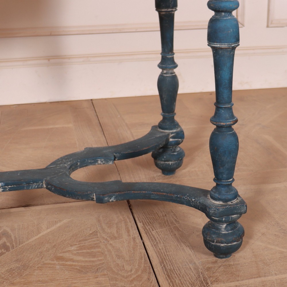 A rectangular blue painted wooden lamp table featuring turned legs, a single drawer with a metal pull, a scalloped apron, and a curved X-shaped stretcher. View V