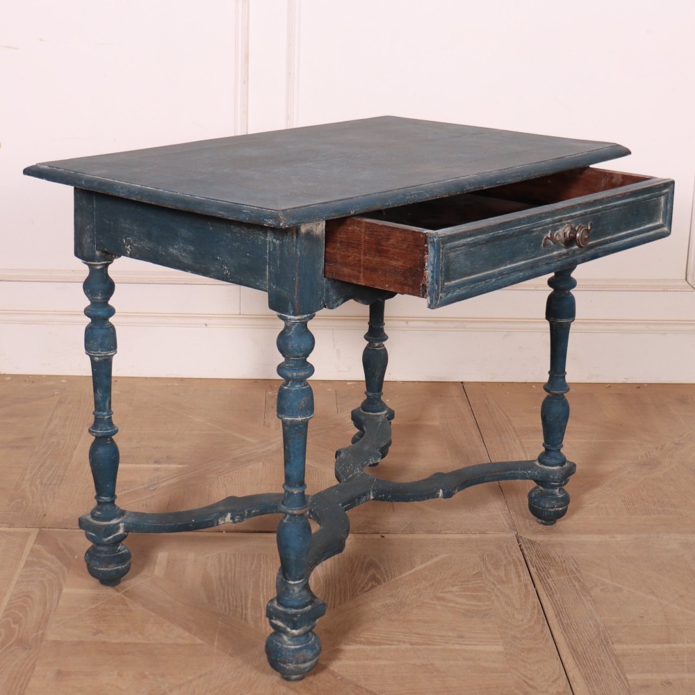 A rectangular blue painted wooden lamp table featuring turned legs, a single drawer with a metal pull, a scalloped apron, and a curved X-shaped stretcher. View VII