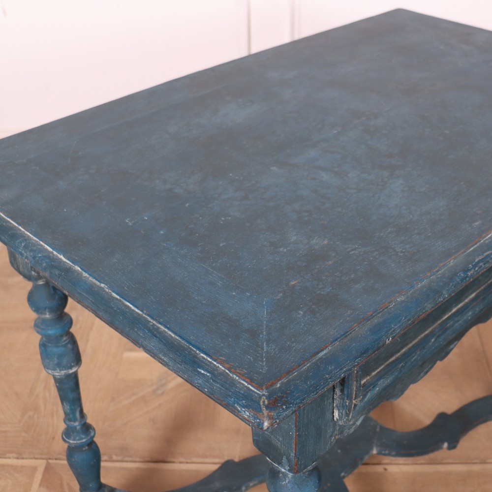 A rectangular blue painted wooden lamp table featuring turned legs, a single drawer with a metal pull, a scalloped apron, and a curved X-shaped stretcher. View VIII