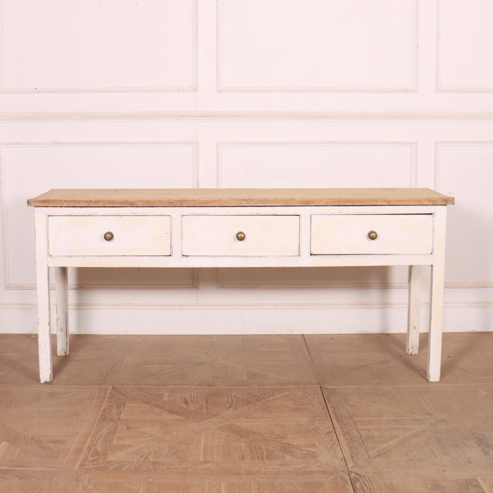 An antique English country dresser base featuring a natural wooden top, three off-white painted drawers with circular brass knobs, and four square straight legs.
