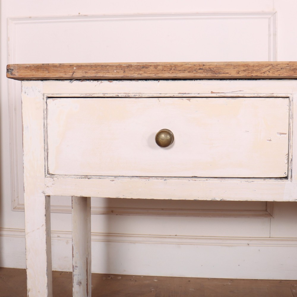 An antique English country dresser base featuring a natural wooden top, three off-white painted drawers with circular brass knobs, and four square straight legs. View II