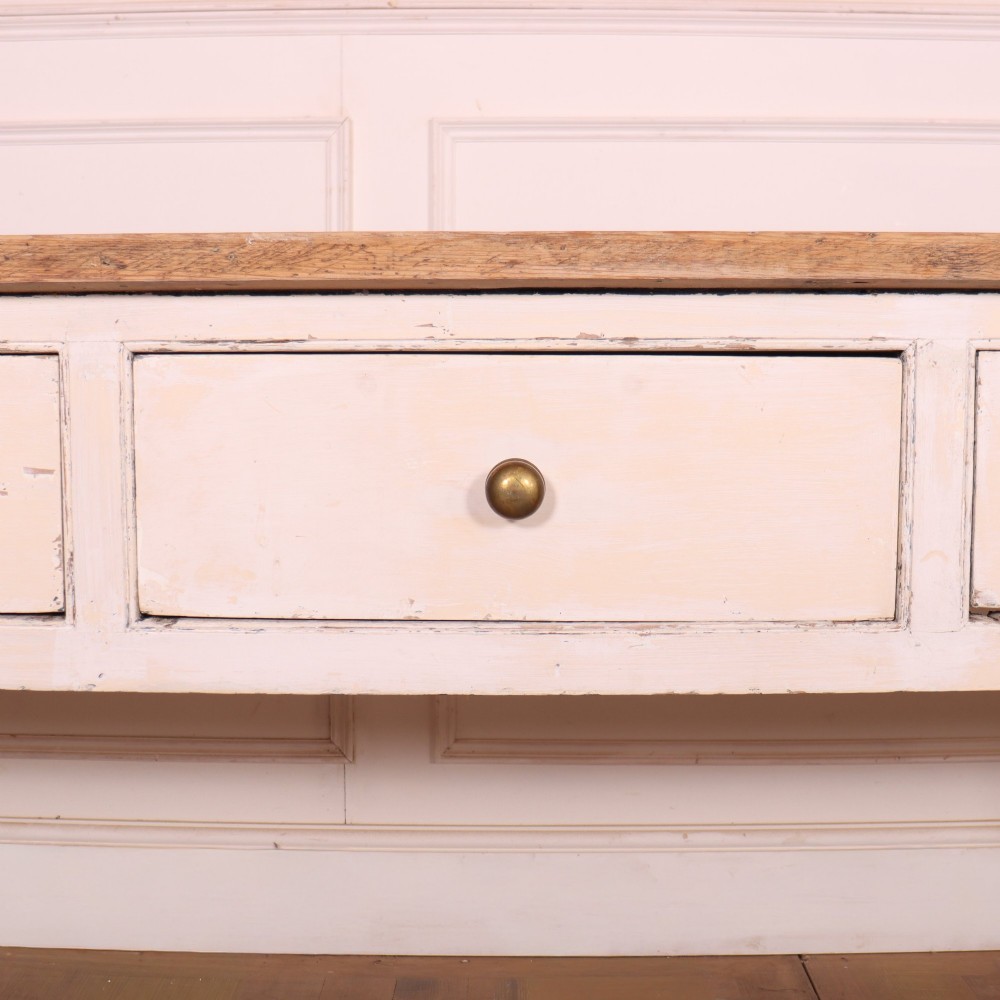 An antique English country dresser base featuring a natural wooden top, three off-white painted drawers with circular brass knobs, and four square straight legs. View IV