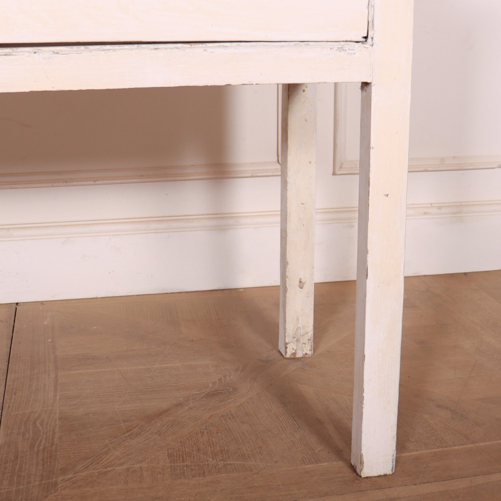 An antique English country dresser base featuring a natural wooden top, three off-white painted drawers with circular brass knobs, and four square straight legs. View VI