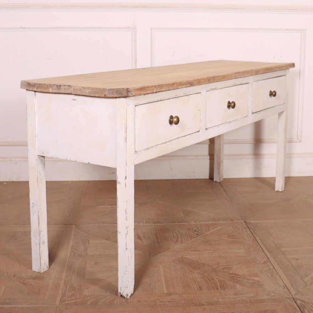 An antique English country dresser base featuring a natural wooden top, three off-white painted drawers with circular brass knobs, and four square straight legs. View VII