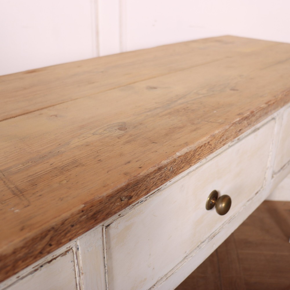 An antique English country dresser base featuring a natural wooden top, three off-white painted drawers with circular brass knobs, and four square straight legs. View X