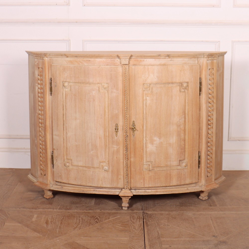 A pale wood bowfront buffet featuring two panelled doors, carved side detailing, and brass keyholes.