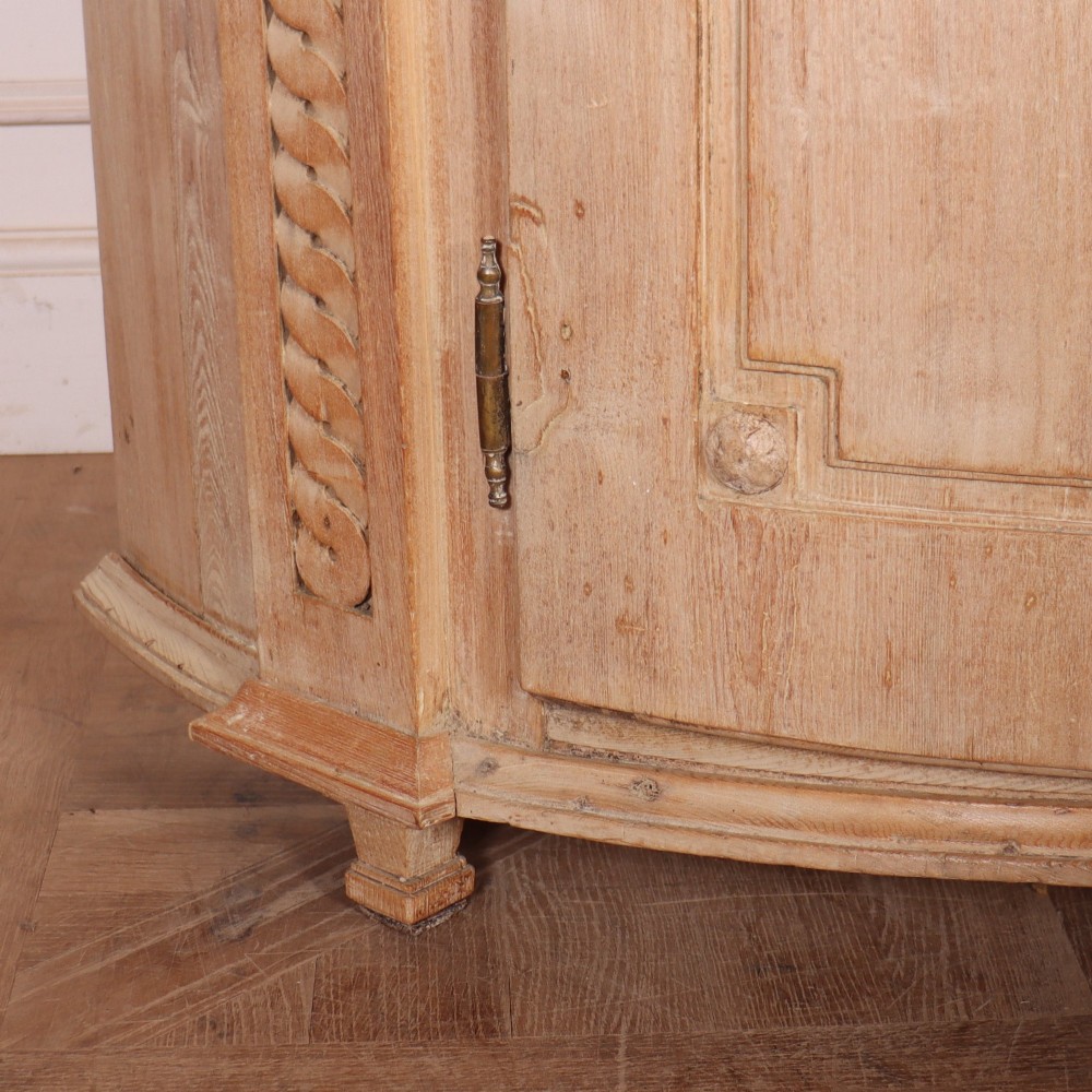 A pale wood bowfront buffet featuring two panelled doors, carved side detailing, and brass keyholes. View III
