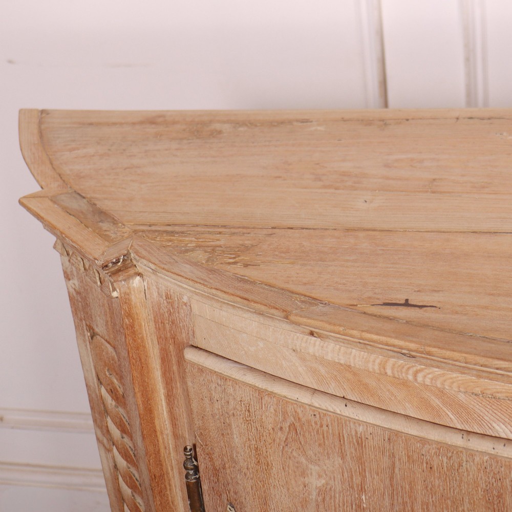 A pale wood bowfront buffet featuring two panelled doors, carved side detailing, and brass keyholes. View VIII