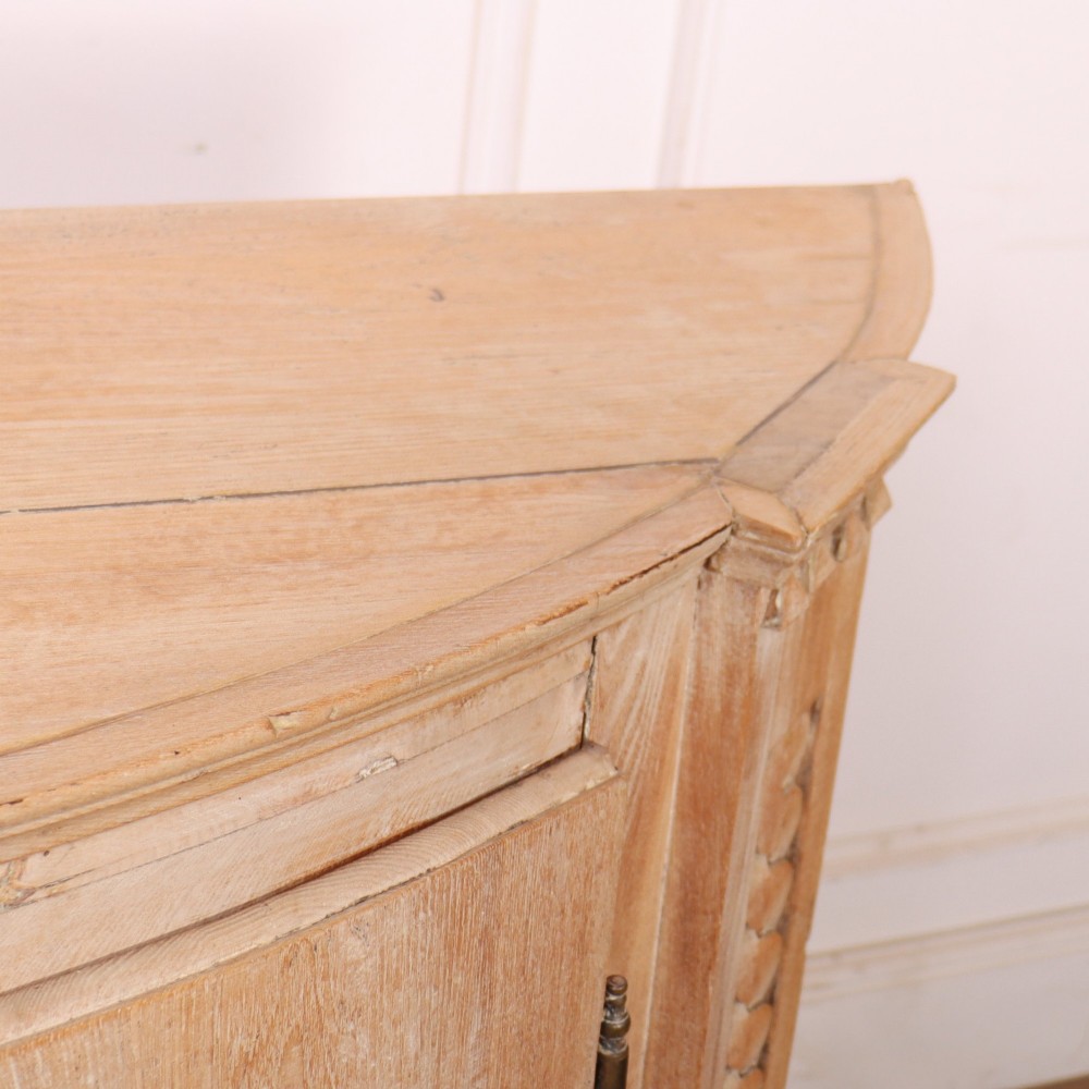 A pale wood bowfront buffet featuring two panelled doors, carved side detailing, and brass keyholes. View IX