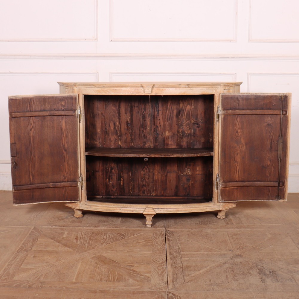 A pale wood bowfront buffet featuring two panelled doors, carved side detailing, and brass keyholes. View X