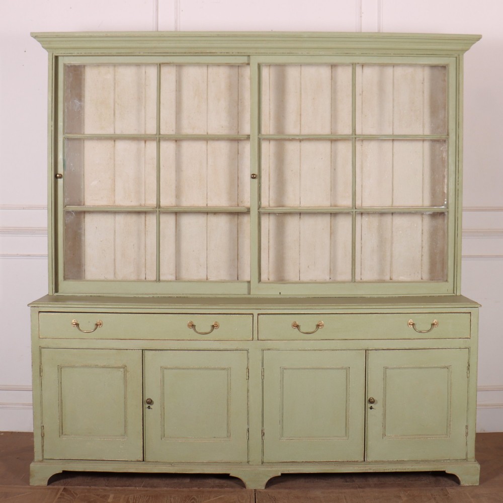 A large sage green painted dresser featuring an upper glazed display cabinet with sliding doors, lower drawers with brass drop handles, and panelled cupboard doors.
