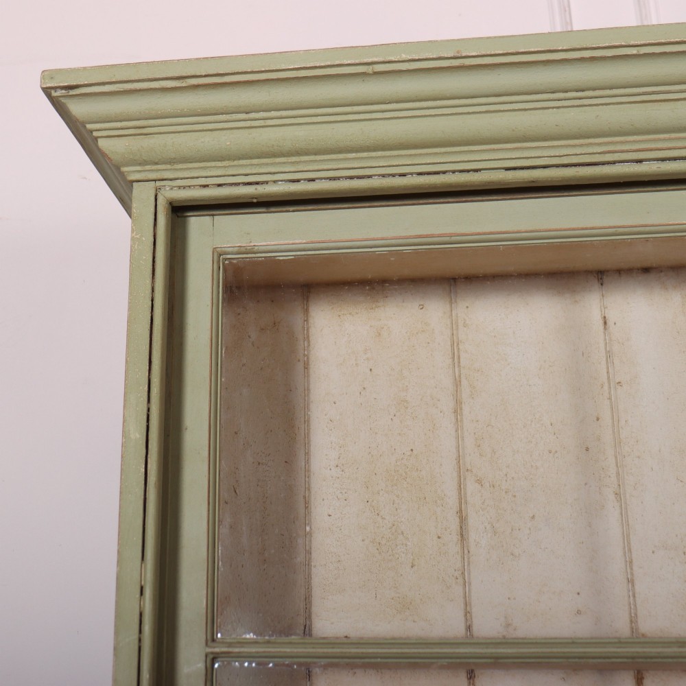 A large sage green painted dresser featuring an upper glazed display cabinet with sliding doors, lower drawers with brass drop handles, and panelled cupboard doors. View II