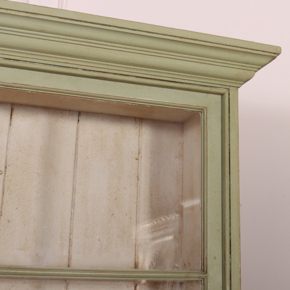 A large sage green painted dresser featuring an upper glazed display cabinet with sliding doors, lower drawers with brass drop handles, and panelled cupboard doors. View IV